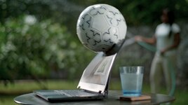 Dell laptop over a table with a glass cup behind the product. A soccer ball is hitting the laptop screen.