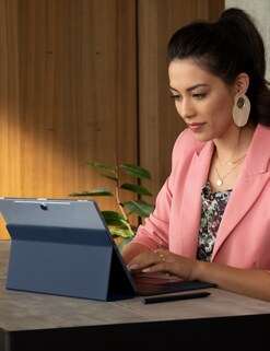 Picture of a woman wearing a pink blazer and typing on a Dell XPS 13 2-in-1 over a table.