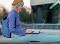 Picture of a sitting woman wearing a purple sweater and backpack using a Dell XPS 13 9315 Laptop leaning on her lap.