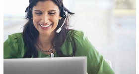 Smiley woman on a green shirt and a headset on her head using a Dell laptop. 