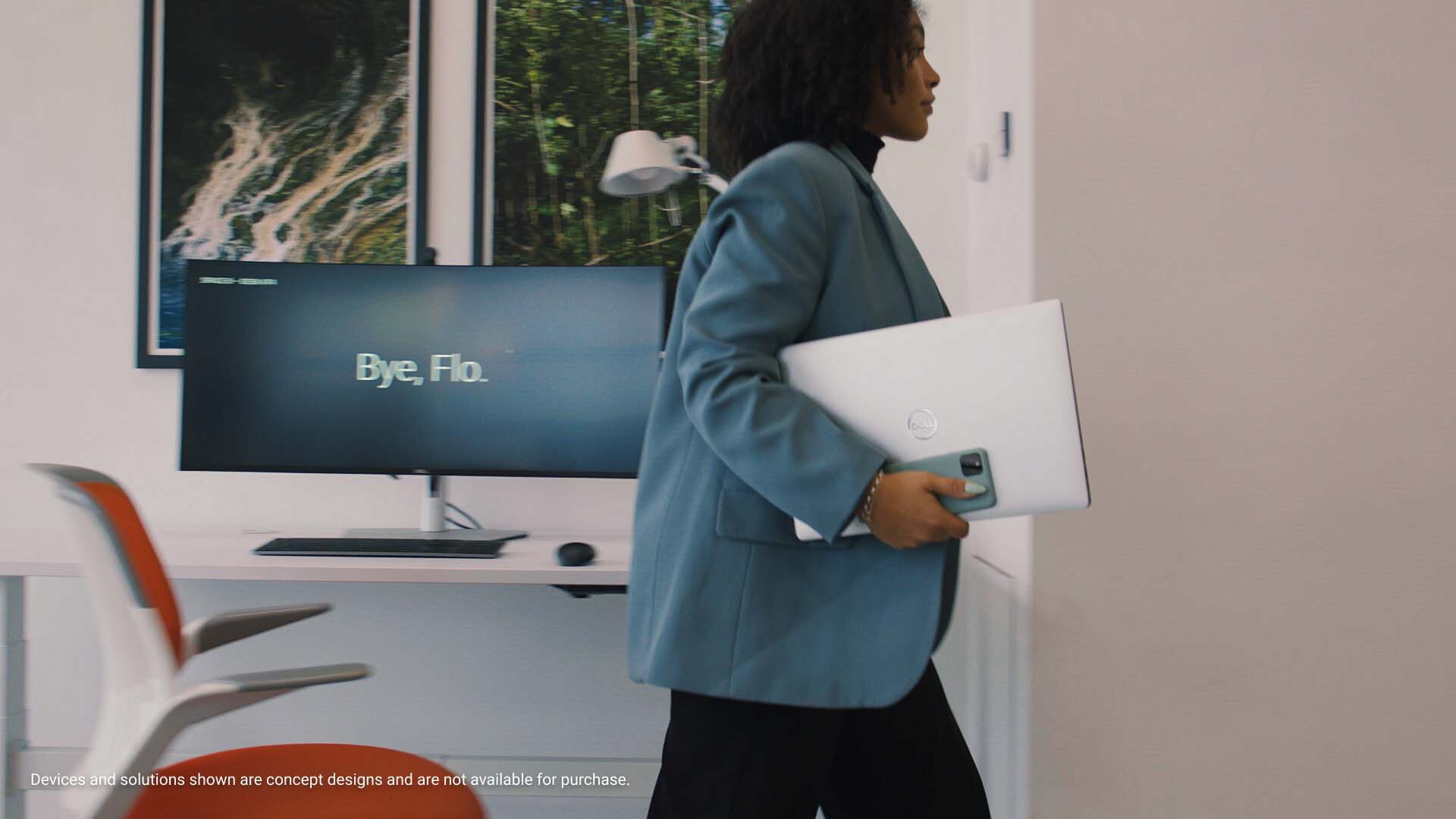 Picture of a woman in a blue suit holding a Dell Laptop and a cell phone walking out of a office room.