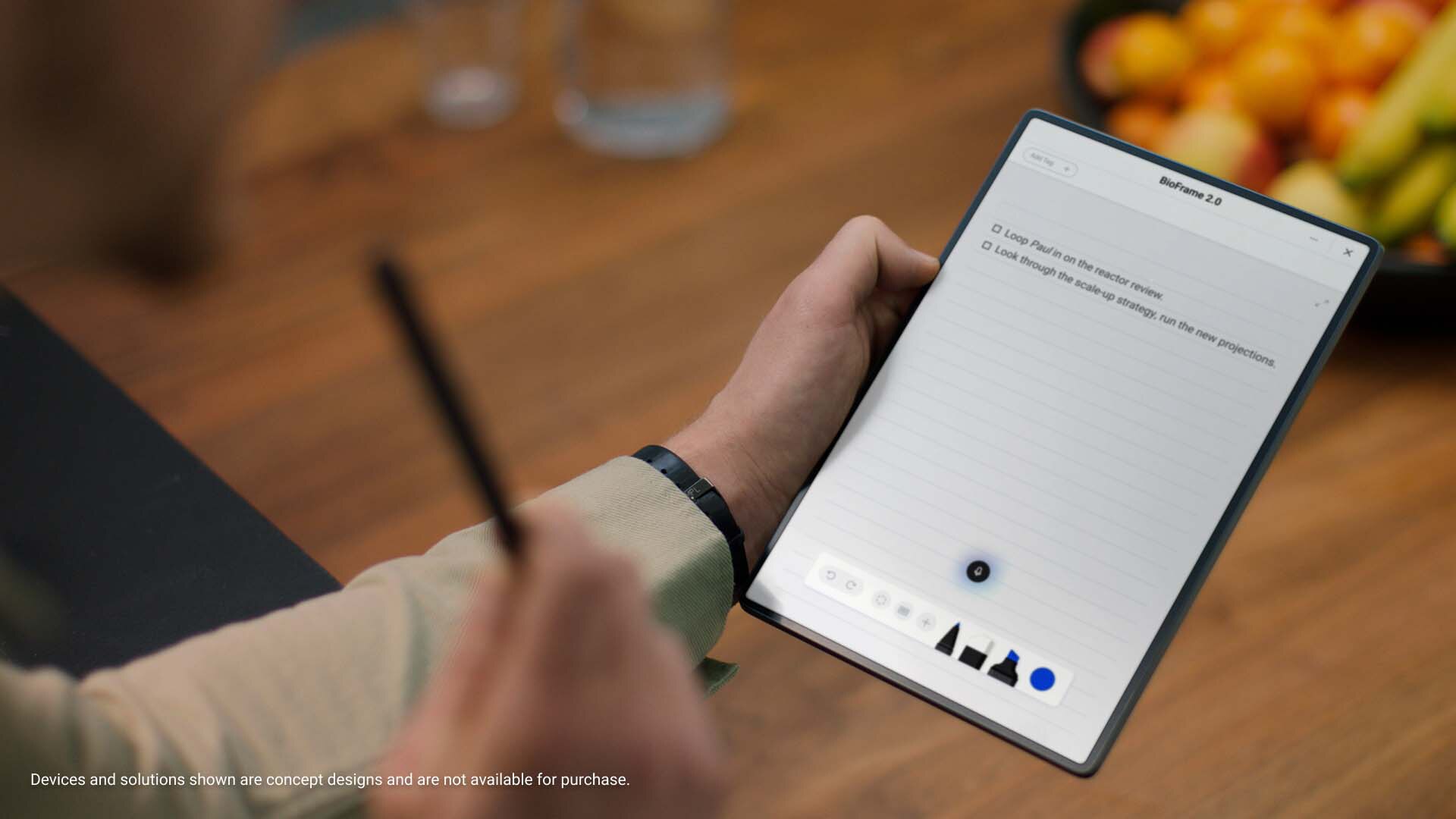Picture of a men left hand holding a concept device that look like a tablet with a notepad and other icons on the screen.