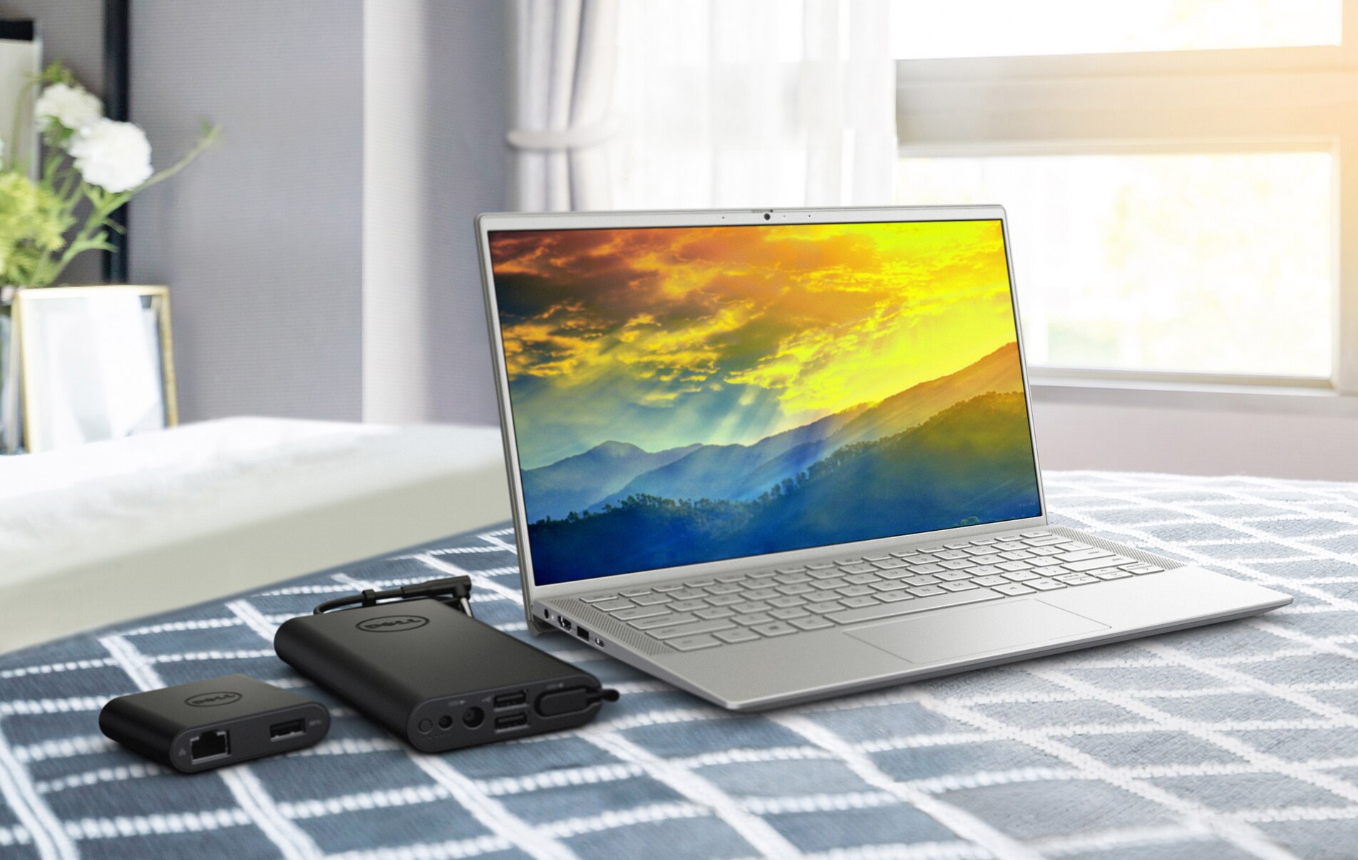 屏幕上显示着彩色背景的戴尔笔记本电脑的图片，产品旁边放着电池充电器。