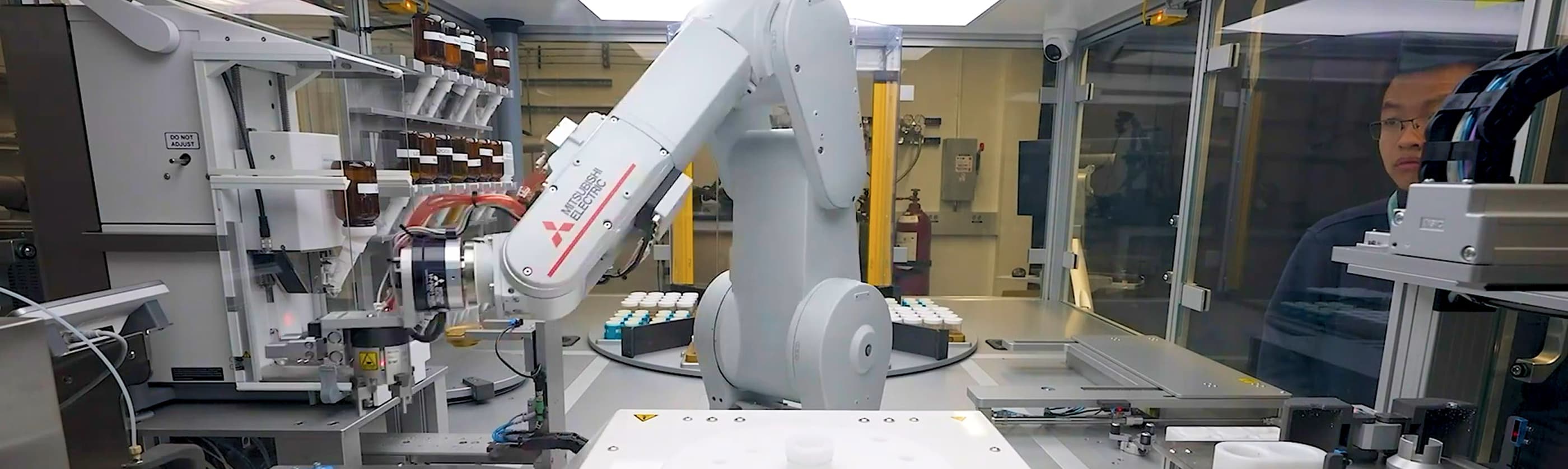 A white industrial robotic arm inside a laboratory automation enclosure handling sample containers and equipment,