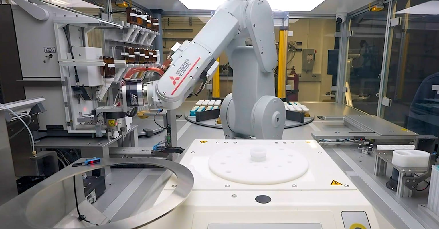 A white industrial robotic arm inside a laboratory automation enclosure handling sample containers and equipment,