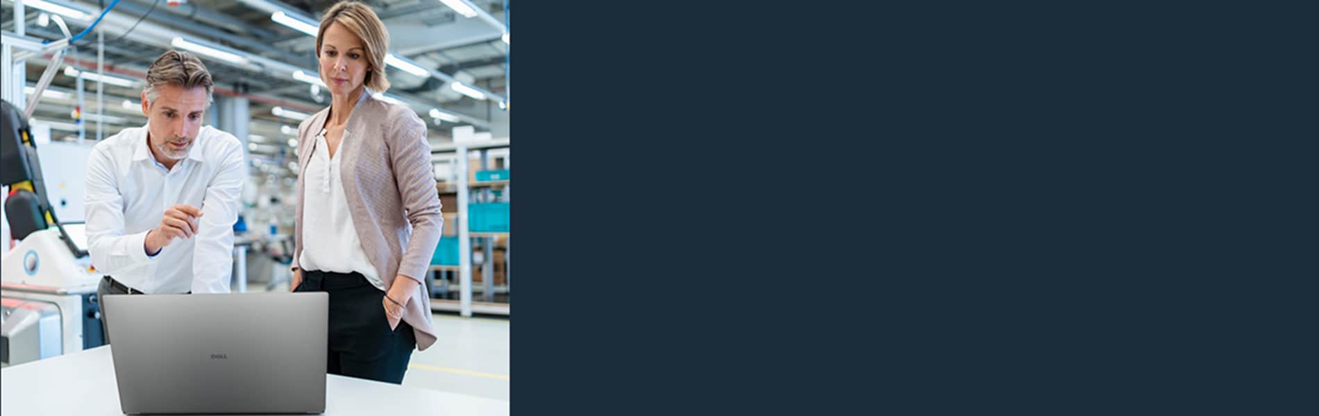 Businessman and businesswoman with laptop talking in a modern factory hall.