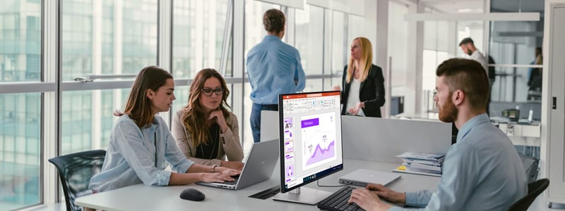 Dell Latitude 5450 Laptop on office desk with charts onscreen, coworkers collaborating nearby.