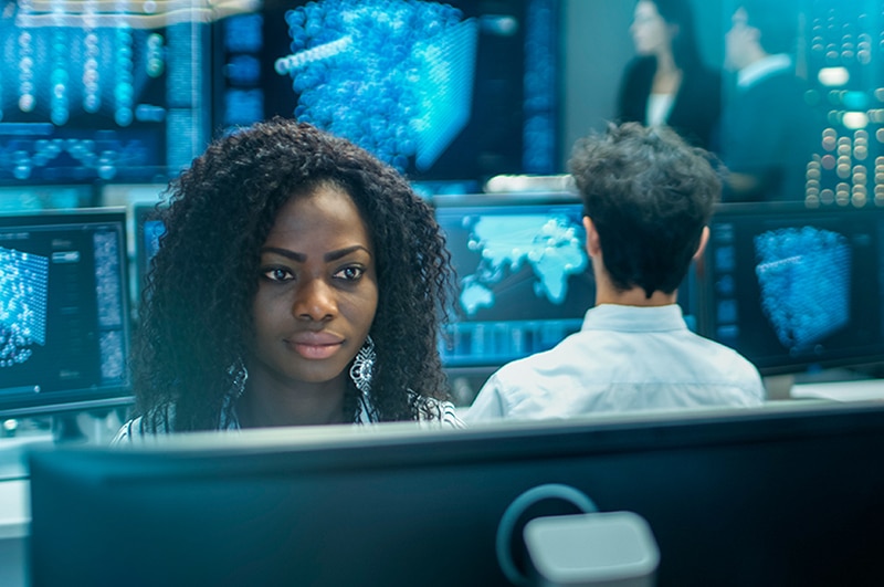 You lady in front of a PC screen in a digital control room with people behind here