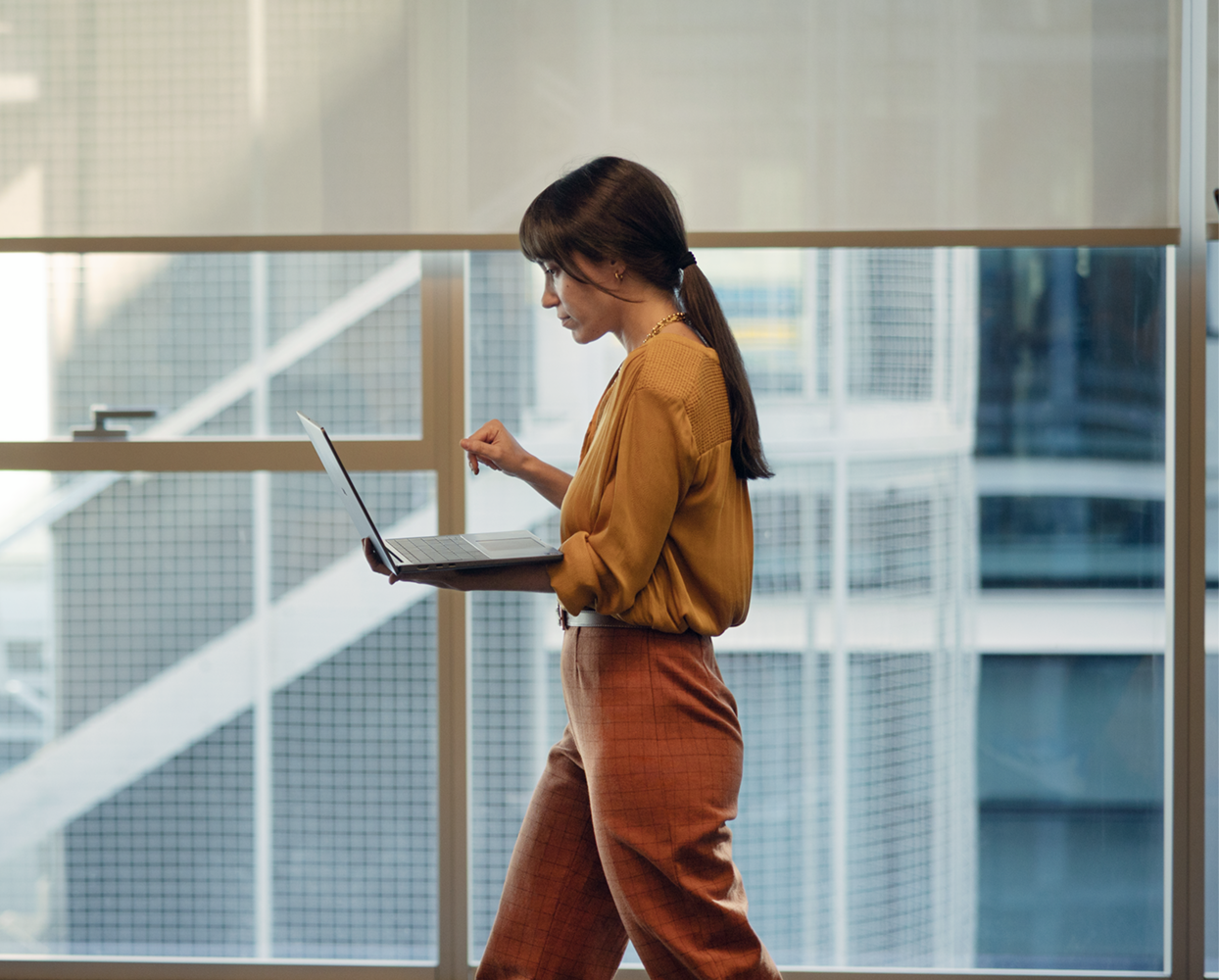 Woman using Dell laptop while walking in a modern office with large windows and natural light.