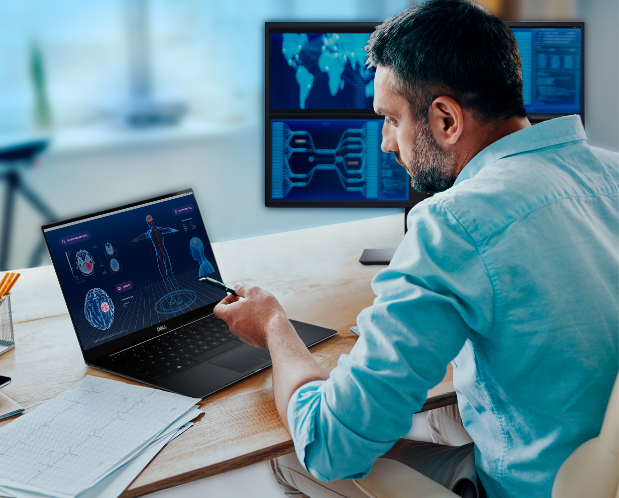 Person reviewing medical graphics on Dell XPS laptop at a desk with dual monitors and charts.
