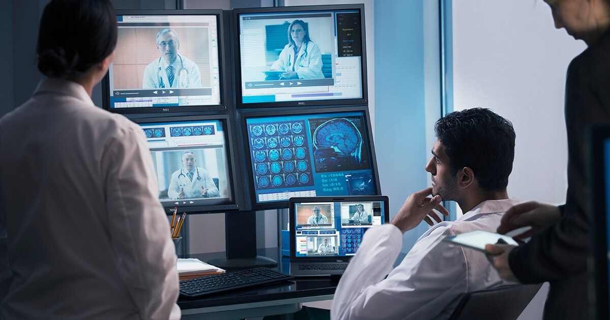 Three medical professional are viewing multiple screens in an office setting.
