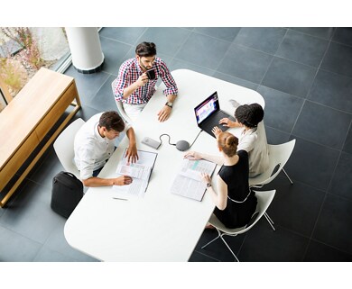 Zdjęcie grupy osób wokół białego stołu z produktami firmy Dell, w tym z zestawem głośnomówiącym Dell MH3021P.