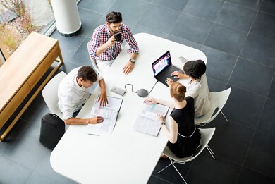 Imagem de um grupo de pessoas em torno de uma mesa branca com produtos Dell, inclusive um viva-voz Dell MH3021P.