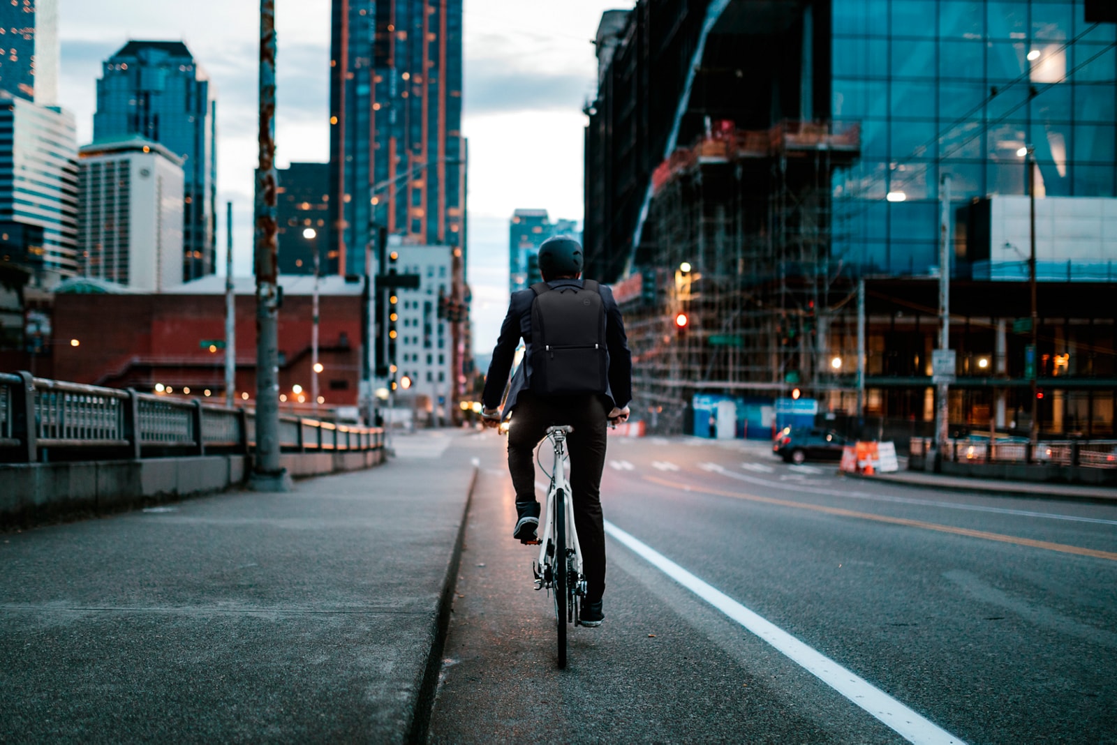 Homem de bicicleta com a cidade diante dele e uma mochila nas costas.