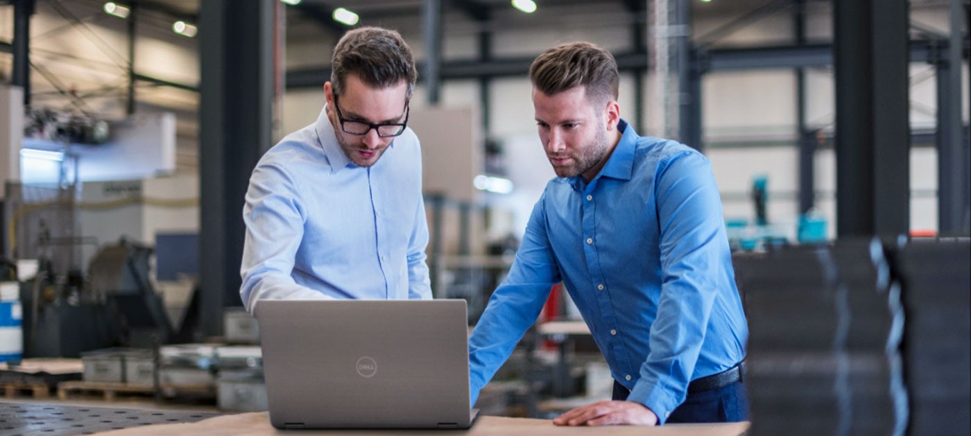 Twee zakenmensen die laptop delen op fabrieksvloer