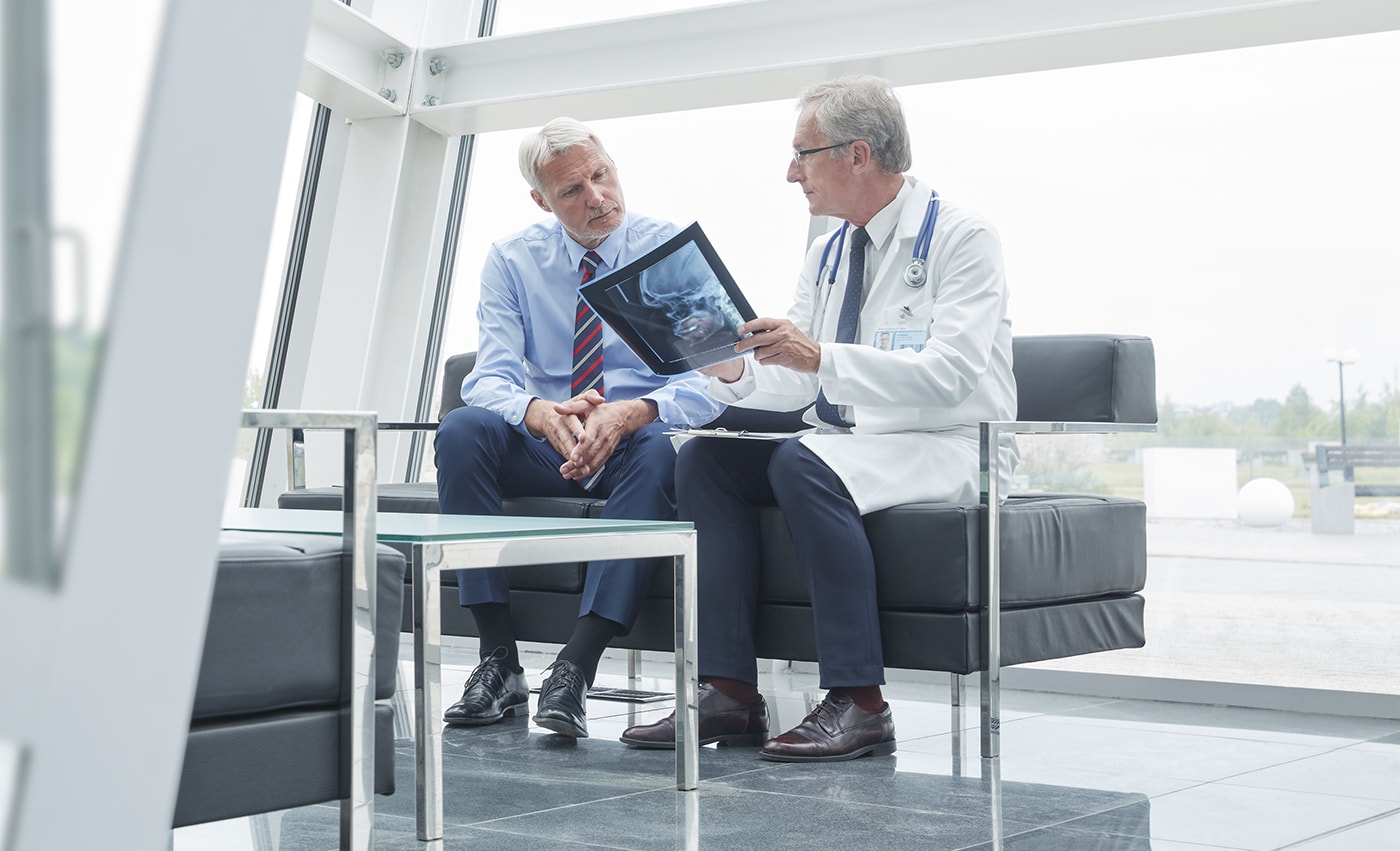 Mandlig kirurg med røntgenbillede, som taler med en patient i hospitalets forhal