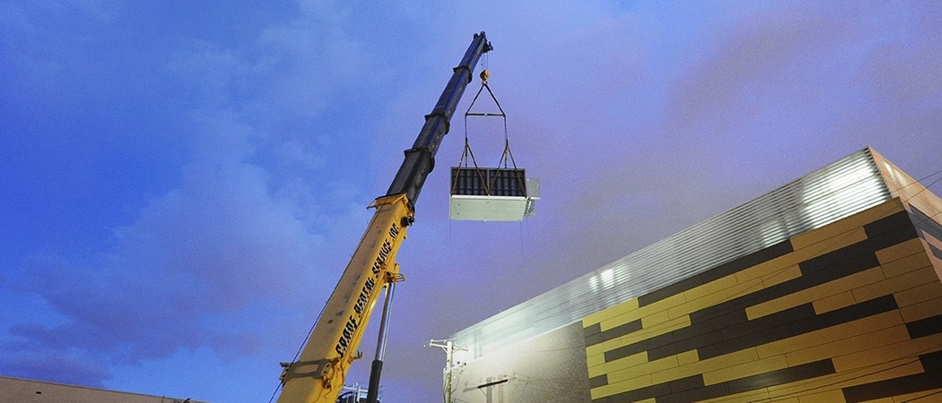 A crane positioning a large modular unit into a building-sized data center.