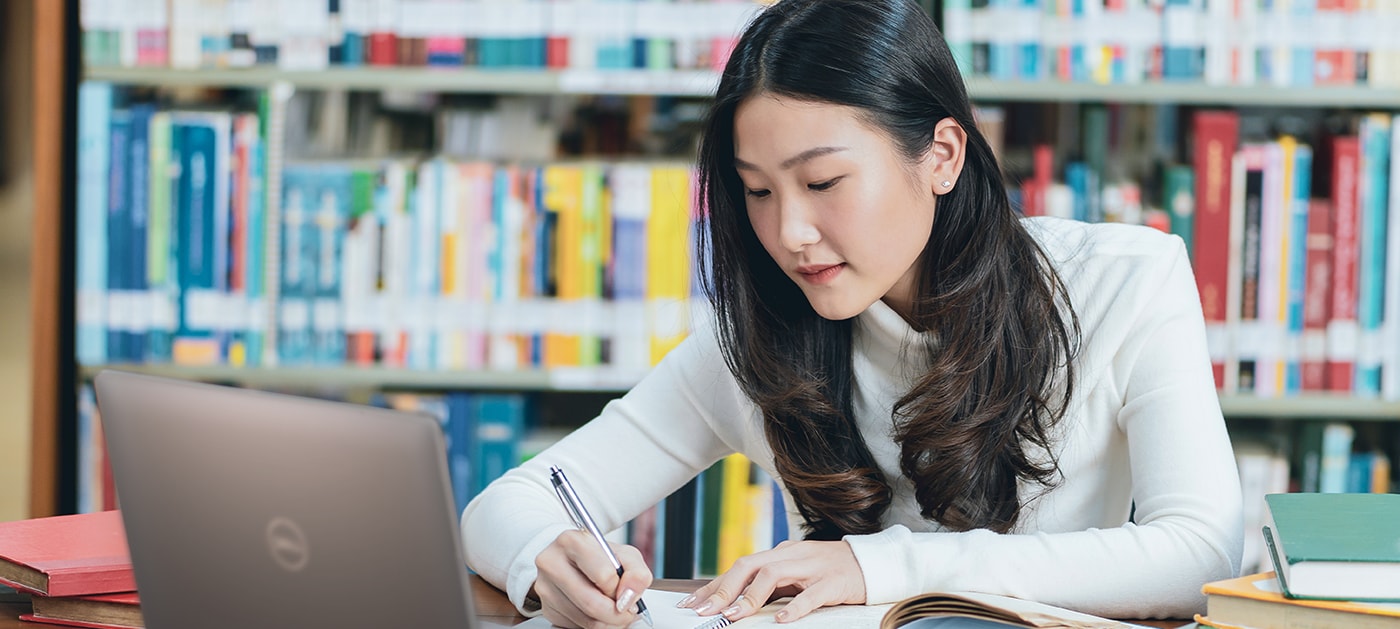 Aziatische vrouwelijke student die op een laptop in bibliotheek werkt