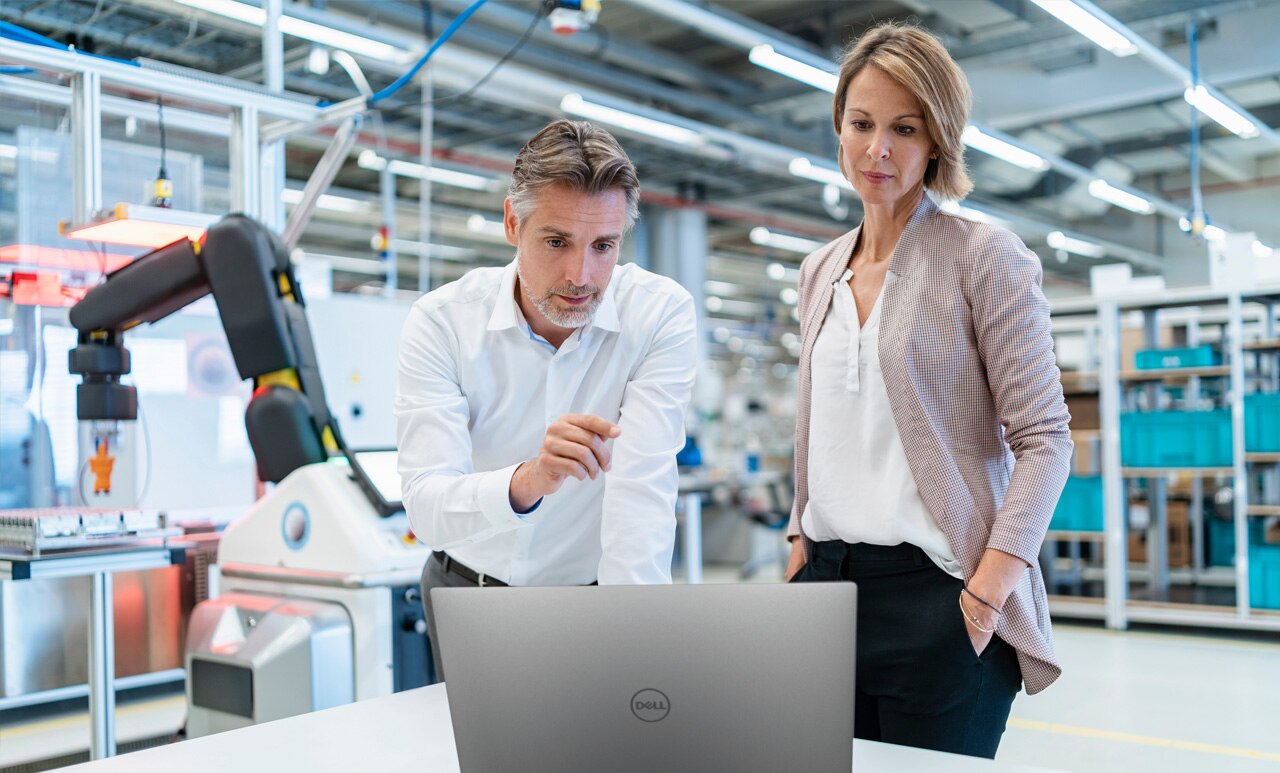 Businessman and Businesswoman with a Laptop Talking in a Modern Factory Hall