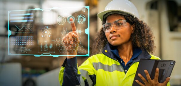 An image of a woman on a jobsite wearing a safety vest and goggles holding a Dell tablet. The woman is interacting with a data display.