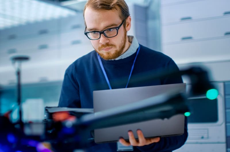 Un jeune ingénieur programme un drone tout en tenant un ordinateur portable