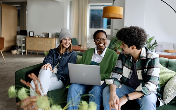 Three smiling people gather around a Dell laptop.