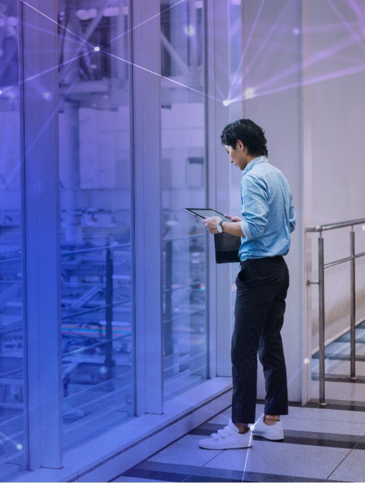Businessman Wearing a Blue Shirt Standing Indoors by Glass Wall Holding a Digital Tablet