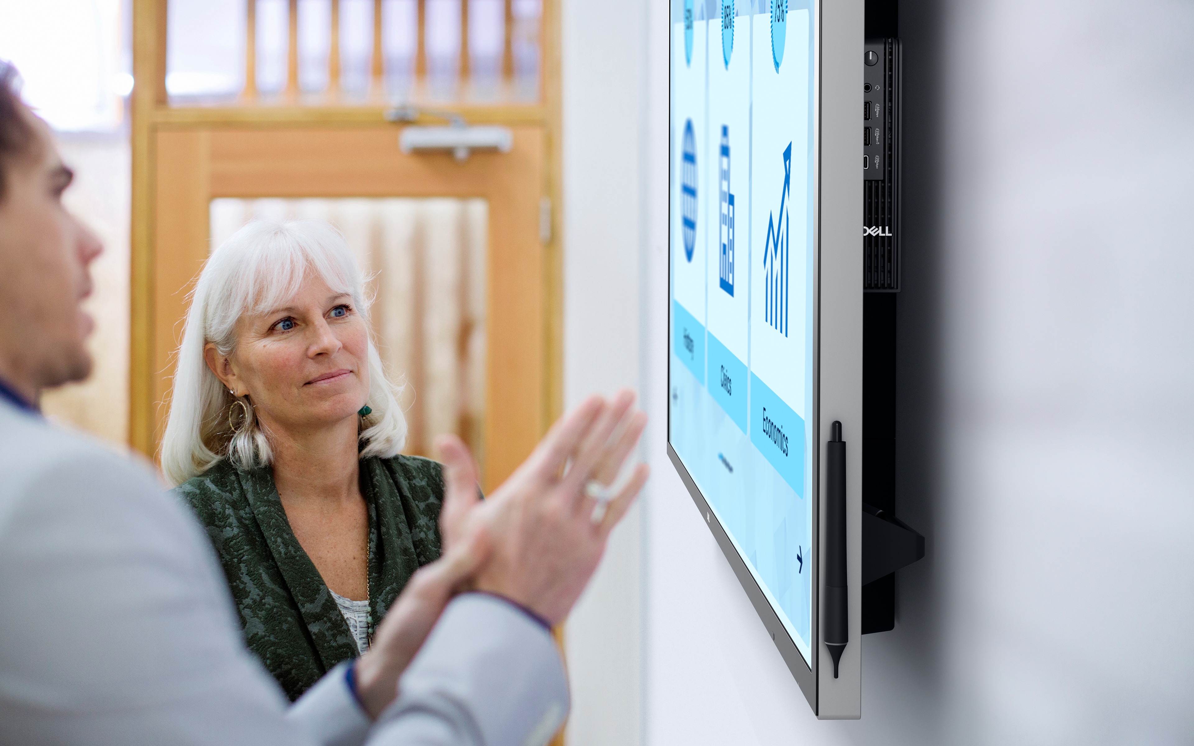 Coworkers discussing items shown on large Dell display.
