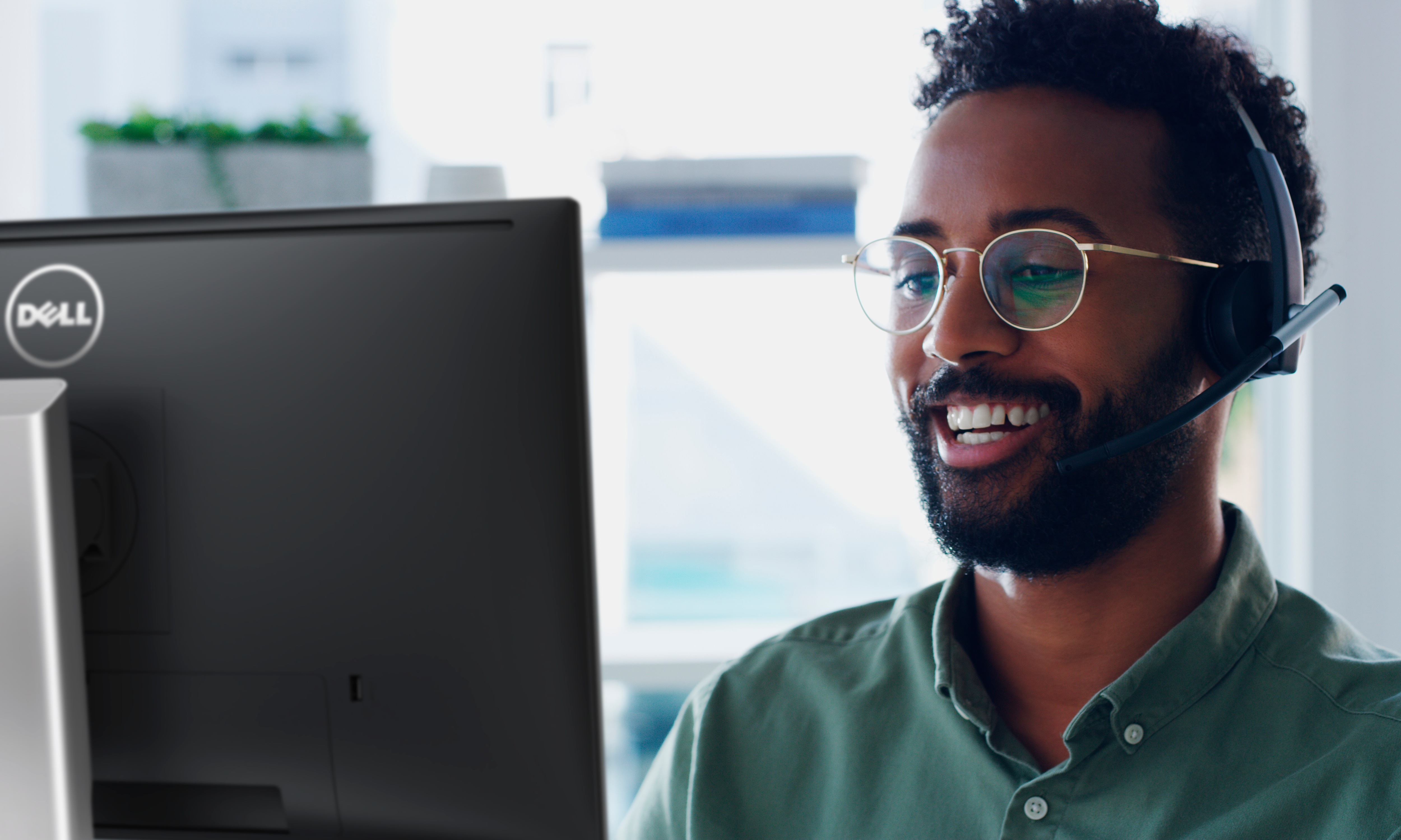 Lachende man met een bril en een headset op zijn hoofd die gebruik maakt van een Dell monitor.