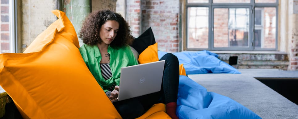 Picture of a woman sitting on a large yellow beanbag chair with a Dell Inspiron 14 5420 Laptop on her lap.