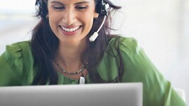 Imagem de uma mulher sorridente com uma camisa verde e um headset na cabeça a utilizar um computador portátil da Dell.