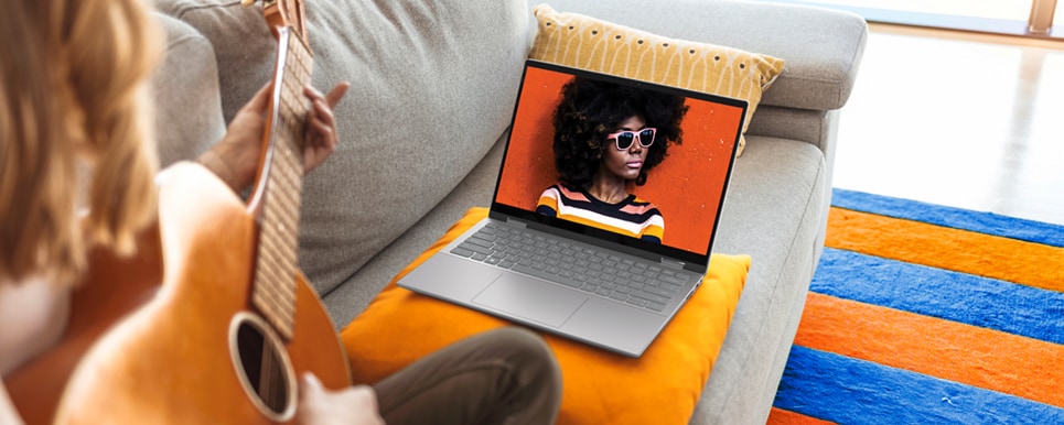 Picture of a Dell Inspiron 14 7420 2-in-1 on an orange pillow in front of a woman playing the guitar.