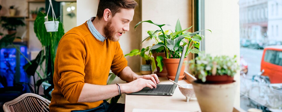 Picture of a men in a yellow sweatshirt using a Dell Inspiron 14 7425 2-in-1 over a wood table among flowerpots.