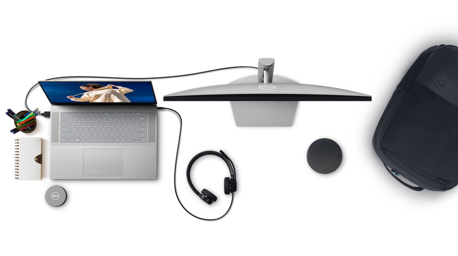 Imagen de una laptop Dell con auriculares y monitor conectados, una mochila, un adaptador móvil y un parlante vistos desde arriba.