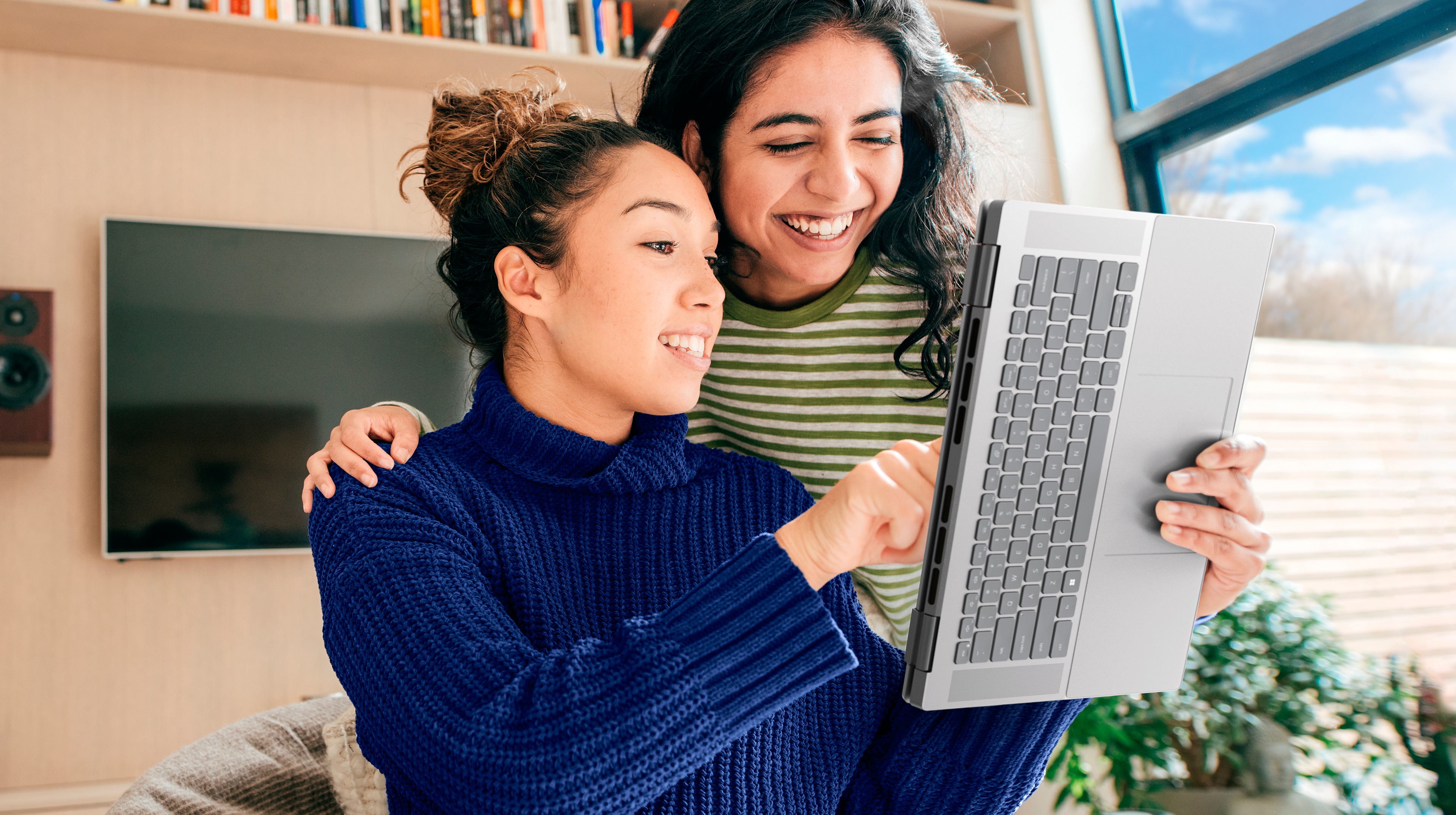 Picture of two girls next to each other, one of them has an Inspiron 7620 2-in-1 opened as a tablet on her left hand.