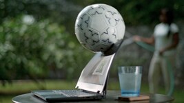 Picture of a Dell laptop over a table with a glass cup behind the product. A soccer ball is hitting the laptop screen.