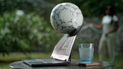Dell laptop over a table with a glass cup behind the product. A soccer ball is hitting the laptop screen.