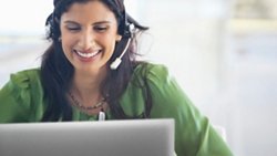 Smiley woman on a green shirt and a headset on her head using a Dell laptop.