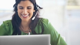 Picture of a smiley woman on a green shirt and a headset on her head using a Dell laptop.