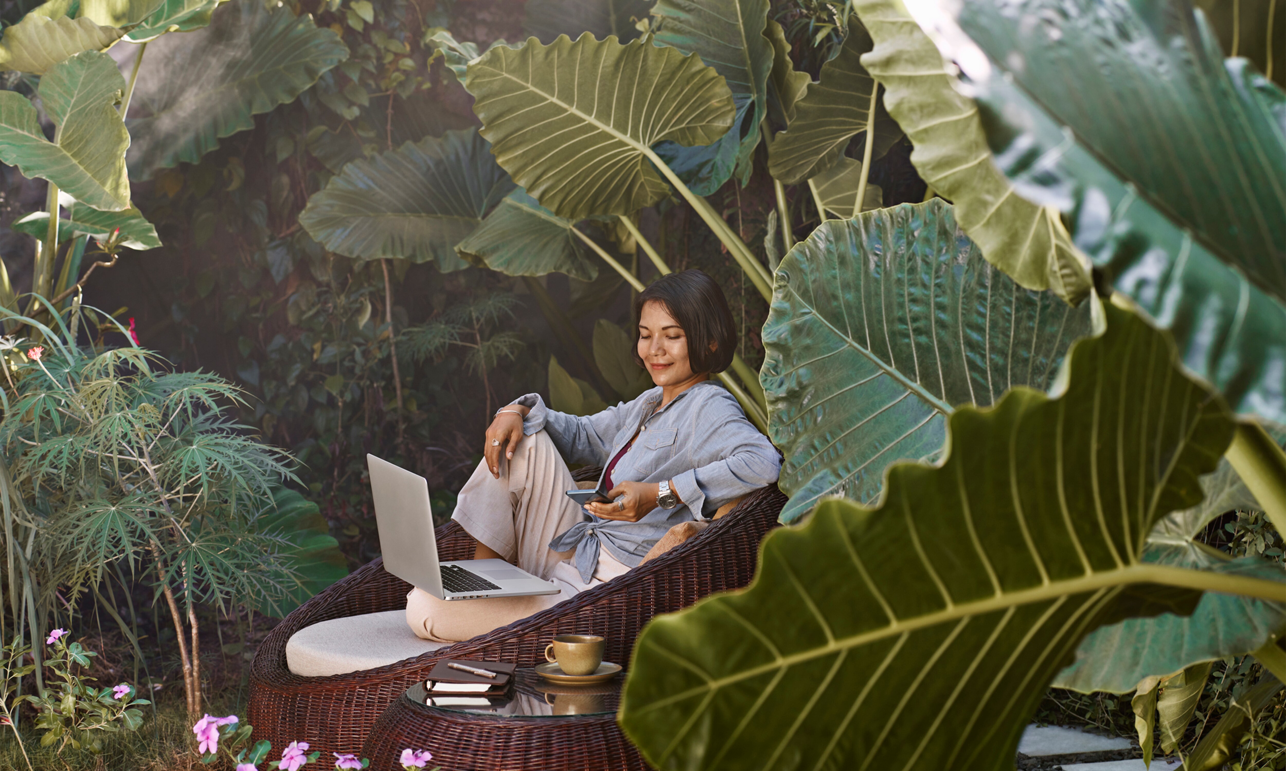 女子坐在椅子上，使用大腿上的 Dell Vostro 5640 筆記型電腦，四周充滿綠意。