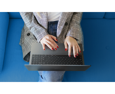 Picture of a woman sitting on a blue sofa with a Dell Vostro 16 5620 Laptop on her lap and her hands on the keyboard.
