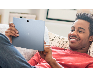 Picture of a smiling man lying on a couch with a Dell XPS 13 9315 2-in-1 Laptop on his hands and wearing a red t-shirt.