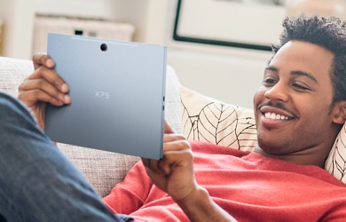 Picture of a smiling man lying on a couch with a Dell XPS 13 9315 2-in-1 Laptop on his hands and wearing a red t-shirt.