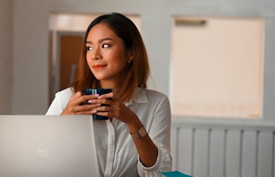 Picture of a woman with a cup in her hands using a Dell XPS 13 2-in-1 9315 laptop on a table in front of her.