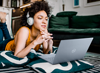 Picture of a woman laying over pillows on the ground with a headset on her head and using a Dell XPS 13 9315 Laptop.