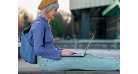 揹著後背包、身著紫色毛衣的女子圖片，她正坐著使用靠在膝上的 Dell XPS 13 9315 筆記型電腦。