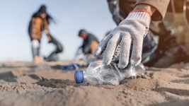 Hand wearing a glove collecting a plastic bottle from the sand