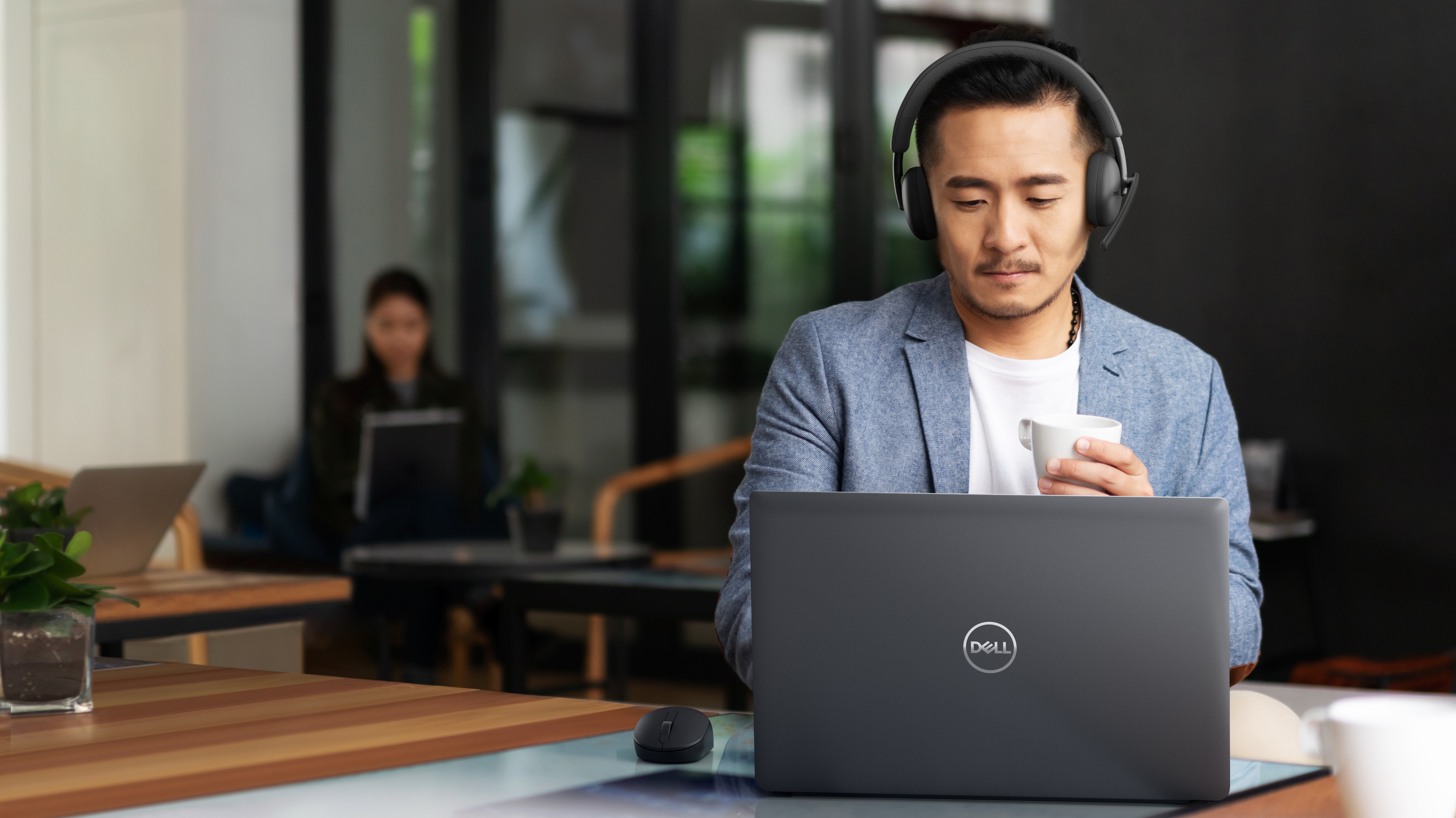 Mann mit Kopfhörer, der an einem Dell Laptop auf dem Tisch vor ihm arbeitet
