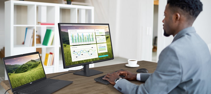 Imagen de un hombre que utiliza productos Dell sobre una mesa, incluido un monitor Dell E2723, un teclado y mouse Dell y una laptop.