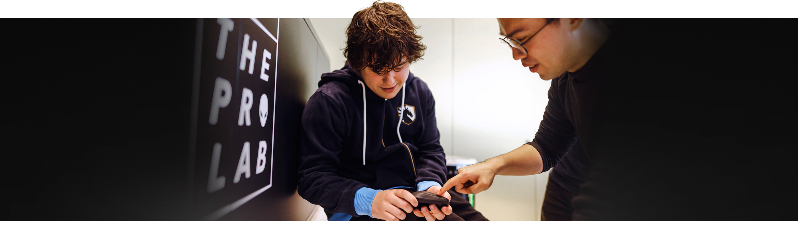 Jeune garçon tenant une souris gaming sans fil Alienware Pro Dell avec un homme à côté qui montre le produit du doigt.